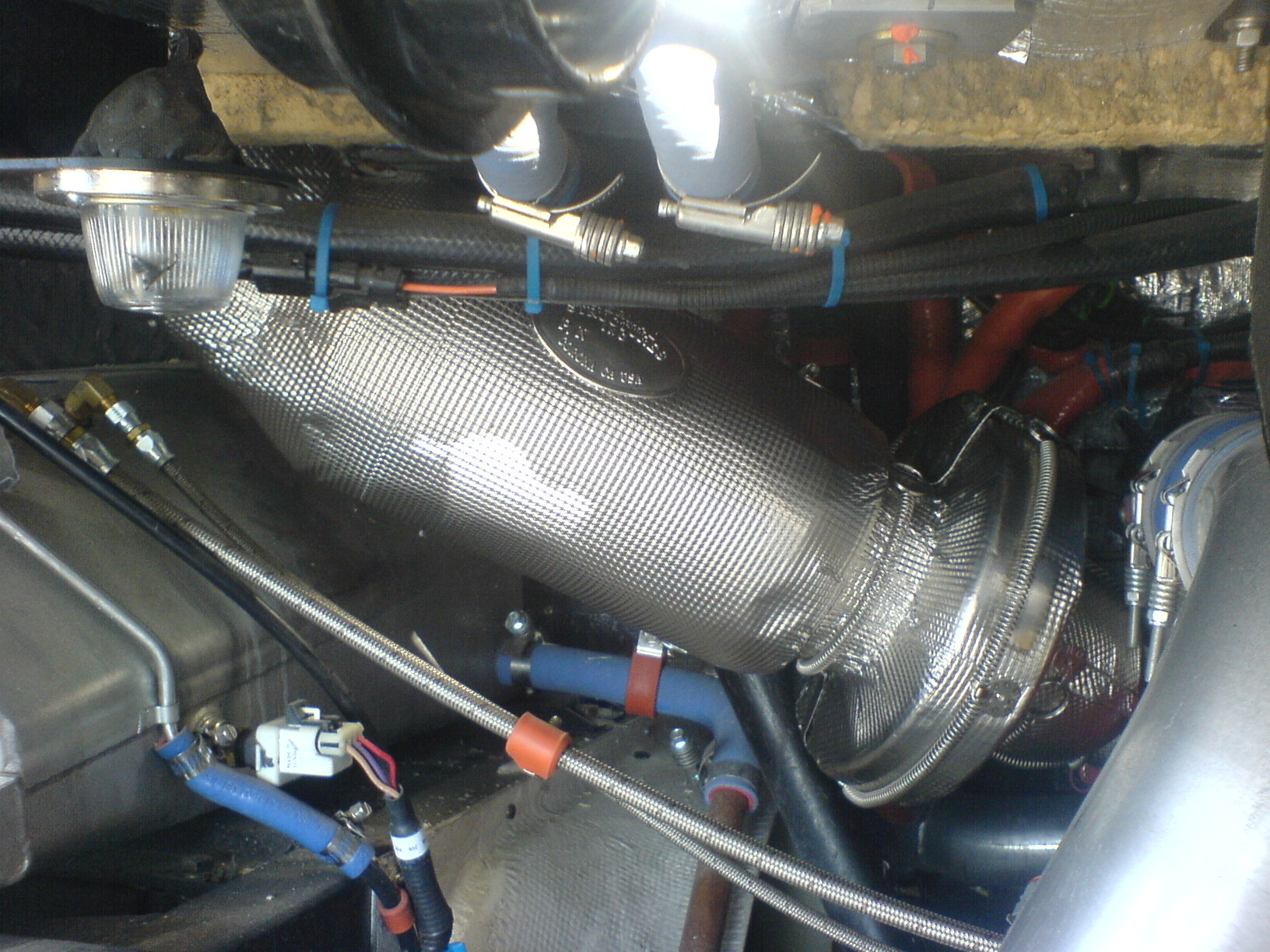 A view of a metal foil insulation blanket over an exhaust bellow within an engine compartment.
