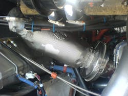 A view of a metal foil insulation blanket over an exhaust bellow within an engine compartment. A view of a metal foil insulation blanket over an exhaust bellow within an engine compartment.