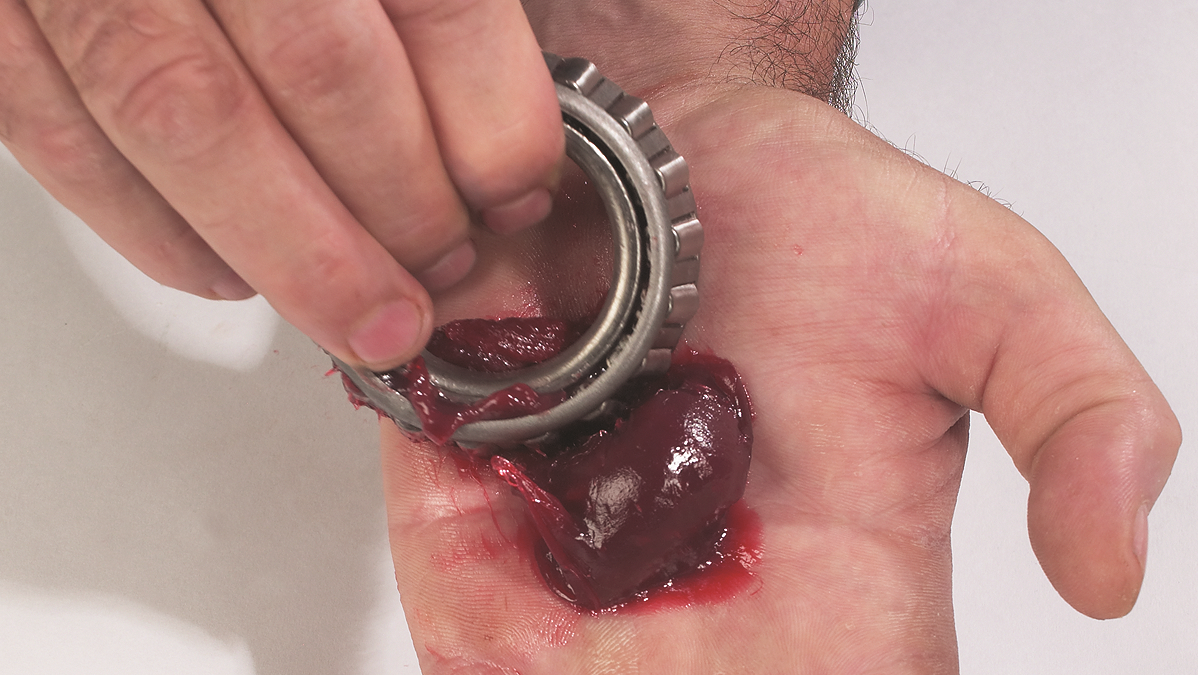 When packing bearings with grease by hand, technicians should start by placing a golf ball size pile of grease into the palm of one hand. Then, using their other hand, push the large end of the bearing cone assembly into the grease.