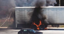 Truck wheels on fire on the side of a highway with firefighters on scene to extinguish the blaze.