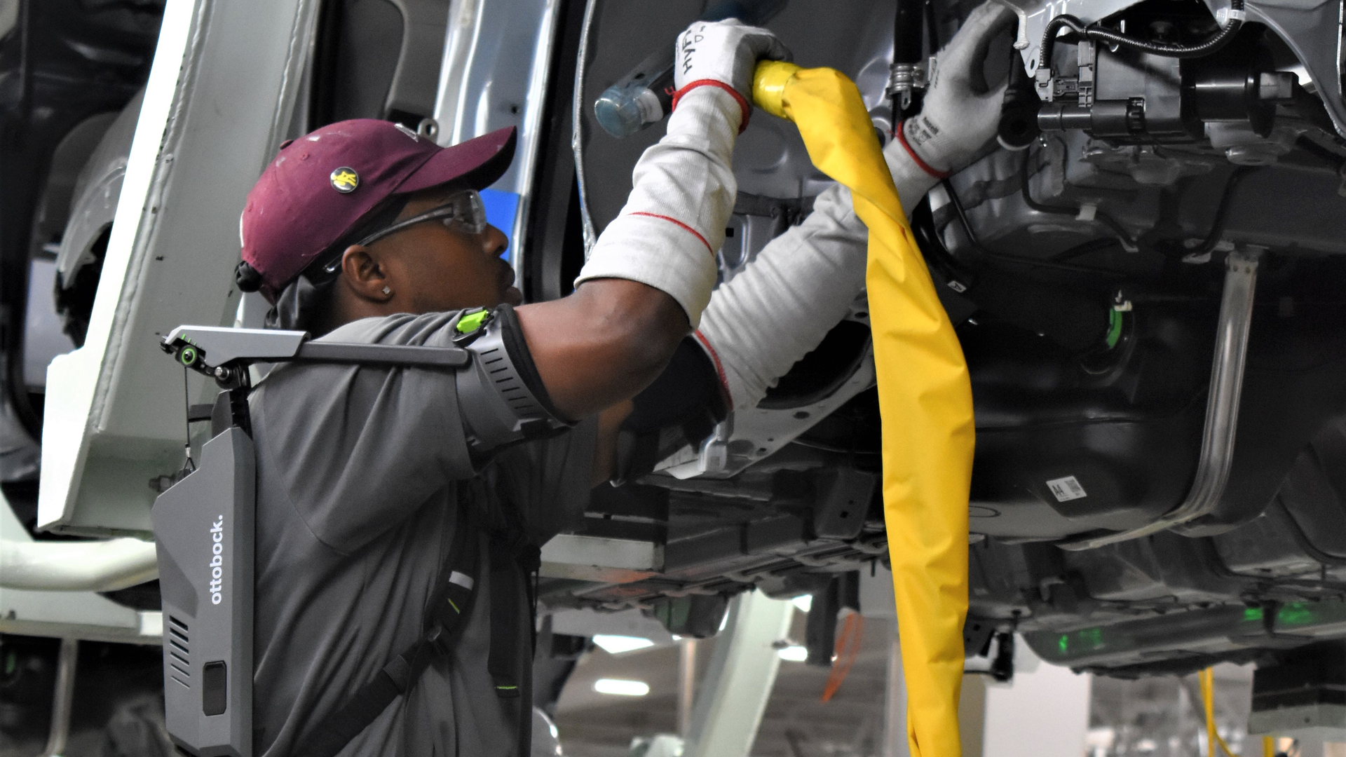 A technician uses an Ottobock Back exoskeleton during repairs, which transfers some of the force bearing down on his shoulders and back to other body parts.