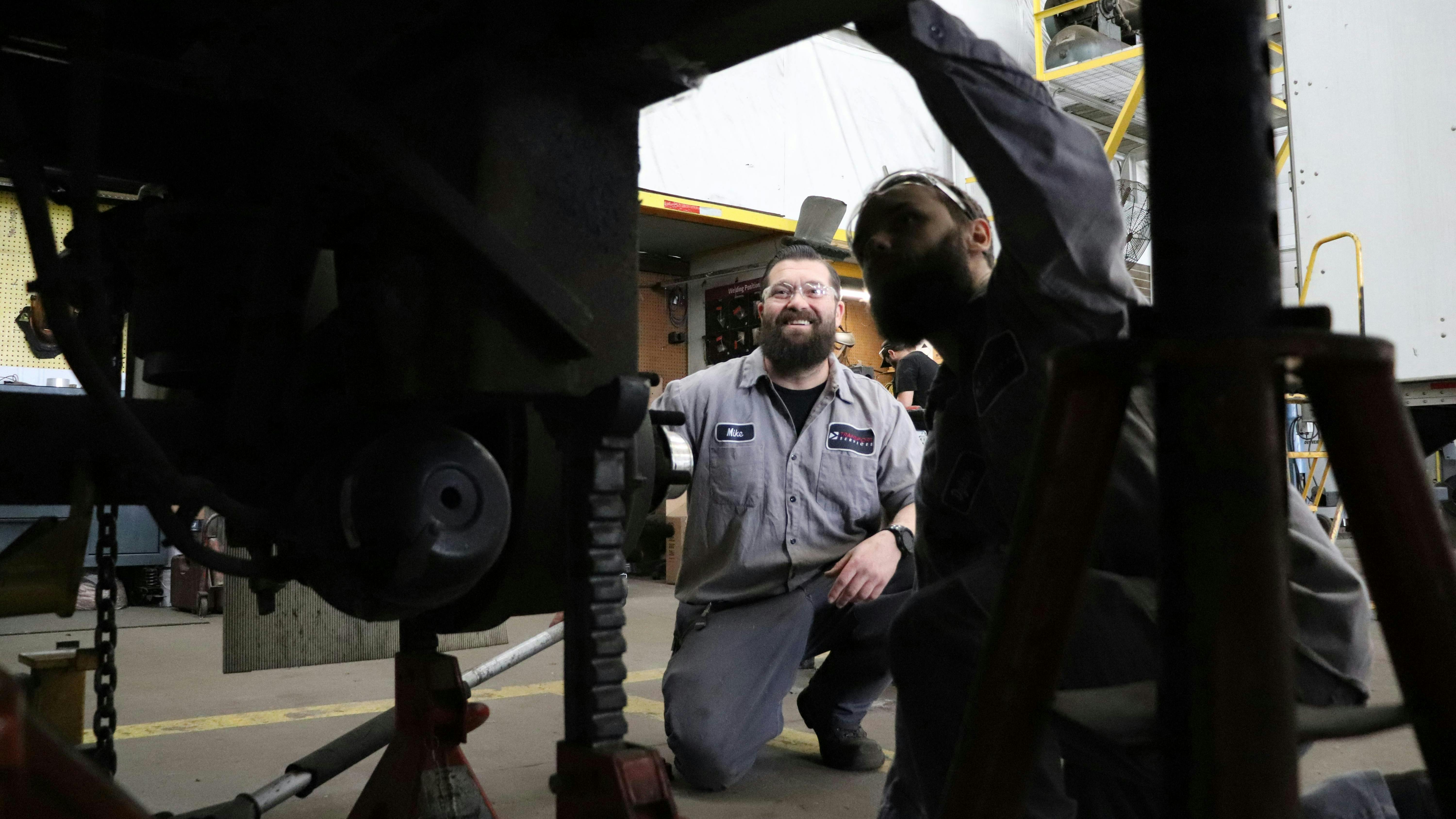 Transport Services technical advisor Mike Conley shows apprentice Dylan Greve how to work on a trailer wheel end.